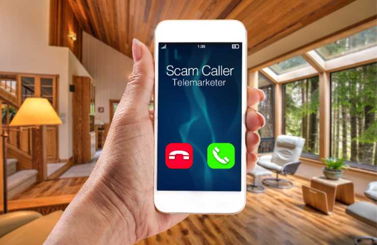 Schermata di chiamata in arrivo su smartphone da numero sospetto con una mano che regge il dispositivo in ambiente living.