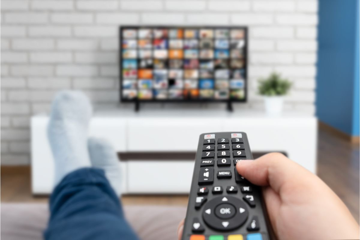 uomo comodo sul divano che cambia canale alla tv