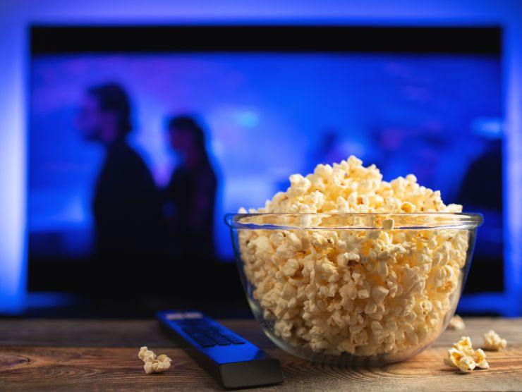 televisore acceso e ciotola con popcorn e telecomando